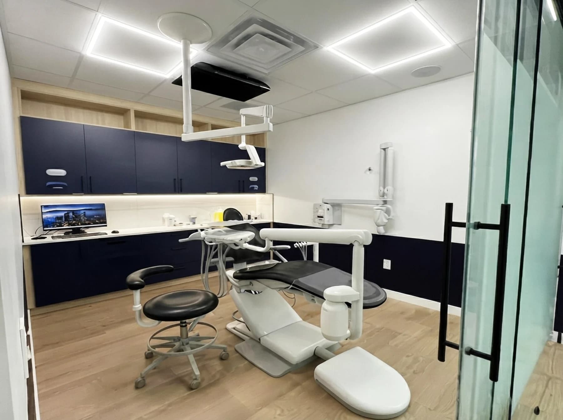 Modern dental treatment room with chair, overhead light, and chairside monitor at Cy Becker Dental